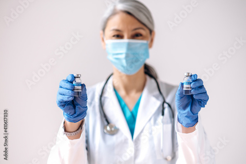A defocused female medical worker  wearing medical mask  holds in hands and ampoules with a coronavirus vaccine  covid19. Vaccination and healthcare concept