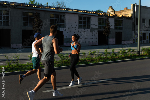 Group of young friends in sports clothing running in city street in morning. 