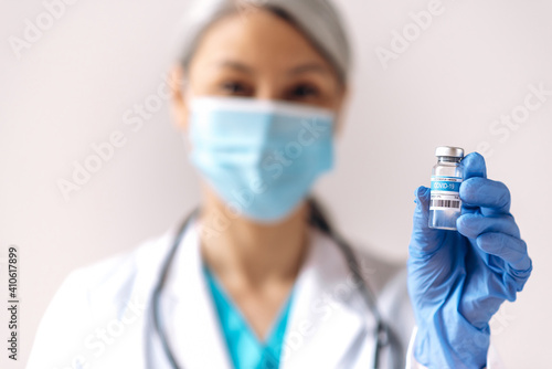 A defocused woman  a medical worker  wearing medical mask  holds an ampule with a coronavirus vaccine  covid19. Vaccination and healthcare concept