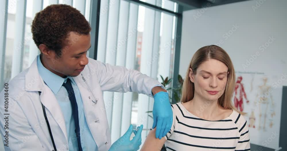 Close up portrait of African American young handsome happy man doctor specialist immunologist injecting beautiful Caucasian joyful woman form coronavirus, disease prevention, vaccination concept Close up portrait of African American young handsome happy man doctor specialist immunologist injecting beautiful Caucasian joyful woman form coronavirus, disease prevention, vaccination concept
