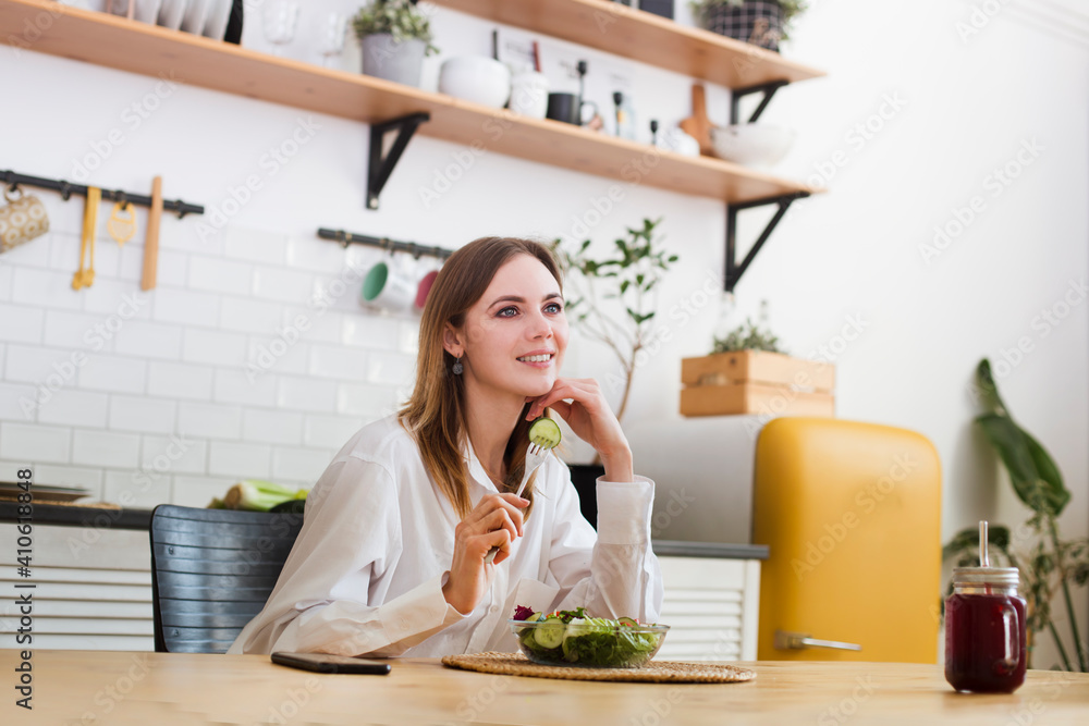 young woman eats green salad for lunch in the kitchen at home