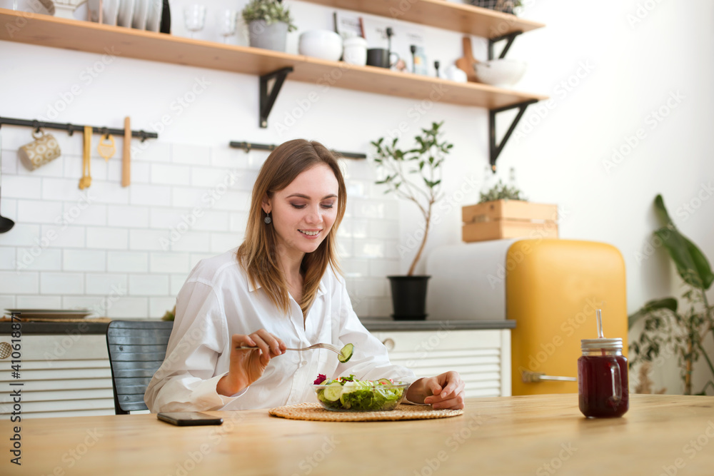 young woman eats green salad for lunch in the kitchen at home