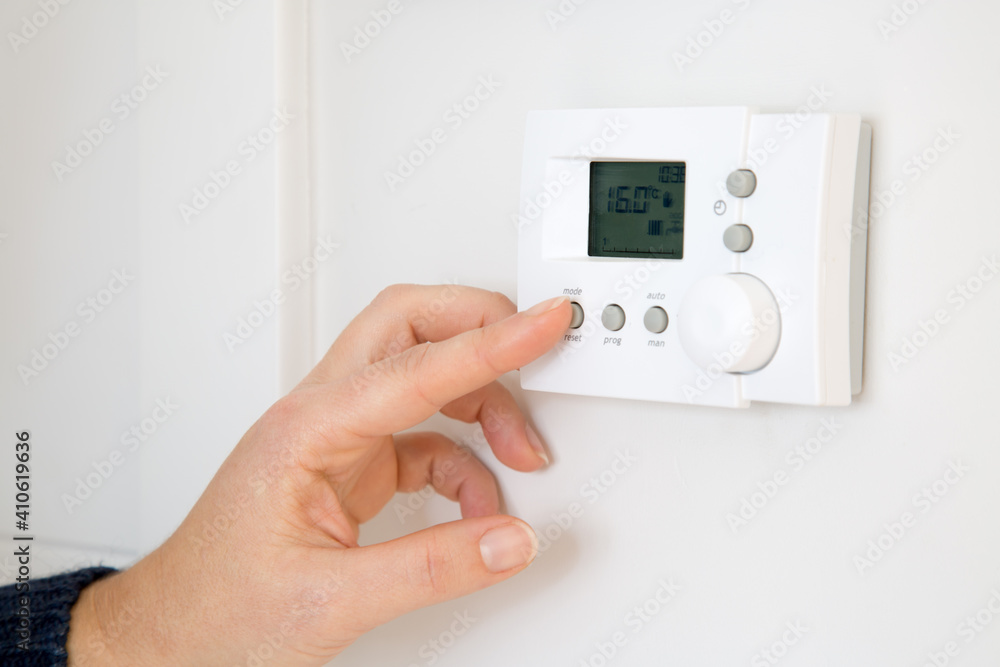 Woman adjusting digital central heating thermostat at home Woman adjusting digital central heating thermostat at home