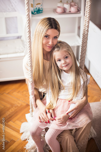 Portrait of mother and daughter sitting on swing in bedroom.