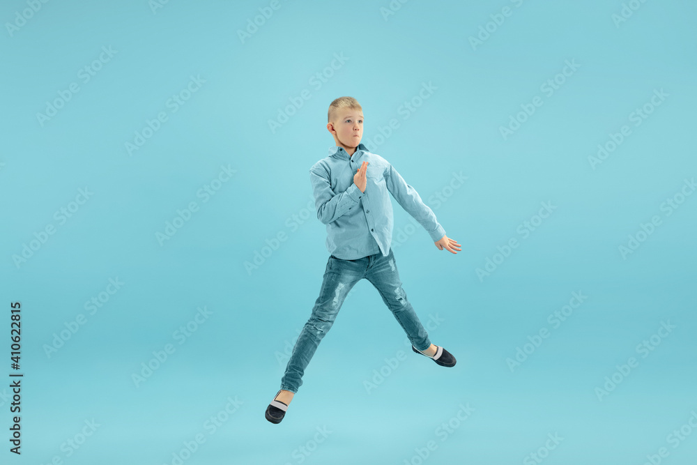 Jumping high. Childhood and dream about big and famous future. Pretty little boy isolated on blue studio background. Childhood, dreams, imagination, education, facial expression, emotions concept.