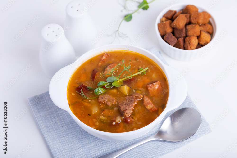 Pea soup with meat, smoked sausage, pea sprouts and croutons. Traditional Russian dish. Home kitchen. Close-up, selective focus. Pea soup with meat, smoked sausage, pea sprouts and croutons. Traditional Russian dish. Home kitchen. Close-up, selective focus.