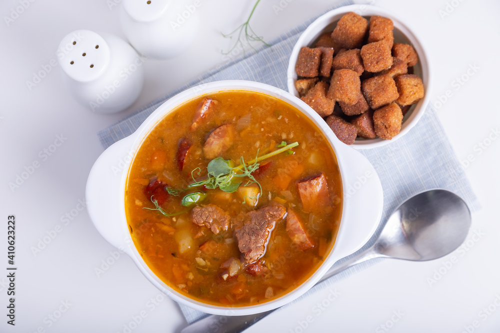 Pea soup with meat, smoked sausage, pea sprouts and croutons. Traditional Russian dish. Home kitchen. Close-up, selective focus. Pea soup with meat, smoked sausage, pea sprouts and croutons. Traditional Russian dish. Home kitchen. Close-up, selective focus.