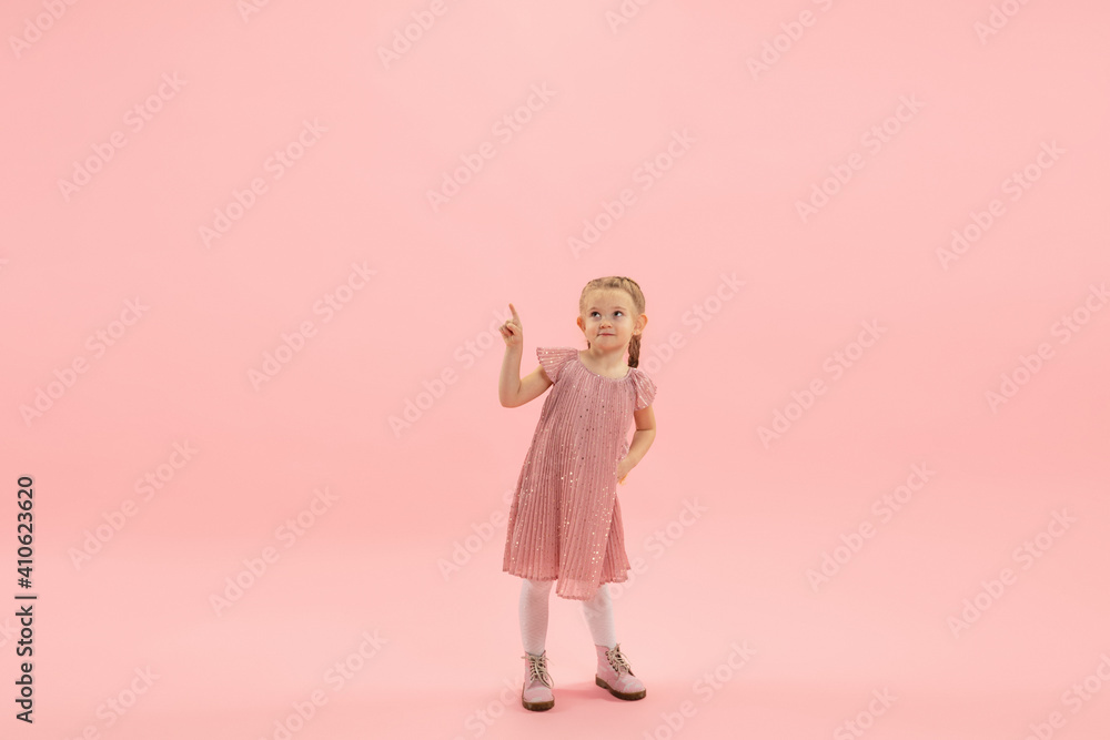 Pointing. Childhood and dream about big and famous future. Pretty longhair girl on coral pink studio background. Childhood, dreams, imagination, education, facial expression, emotions concept. Pointing. Childhood and dream about big and famous future. Pretty longhair girl on coral pink studio background. Childhood, dreams, imagination, education, facial expression, emotions concept.