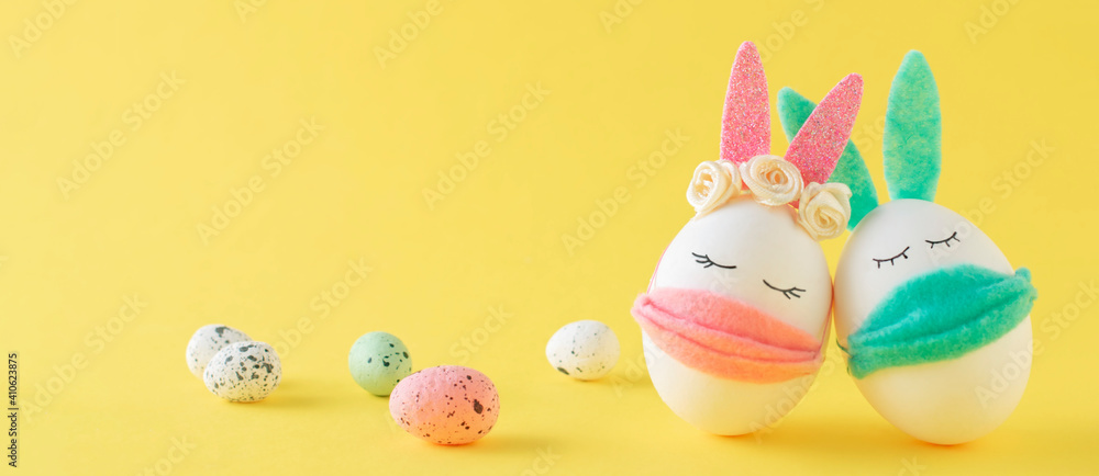  Easter eggs-rabbit  wearing protective masks on a yellow background.  Easter holidays decor. Concept COVID-19, stay home. Banner