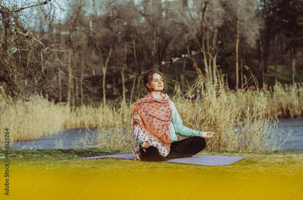 Person sitting in meditation in a park by a lake, lit by sunset light. Concept: self care during pandemic, well-being, outdoor leisure, mental health Person sitting in meditation in a park by a lake, lit by sunset light. Concept: self care during pandemic, well-being, outdoor leisure, mental health