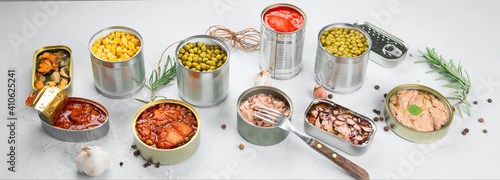 Various canned vegetables, fish and peas in aluminum cans on light gray background. © bit24