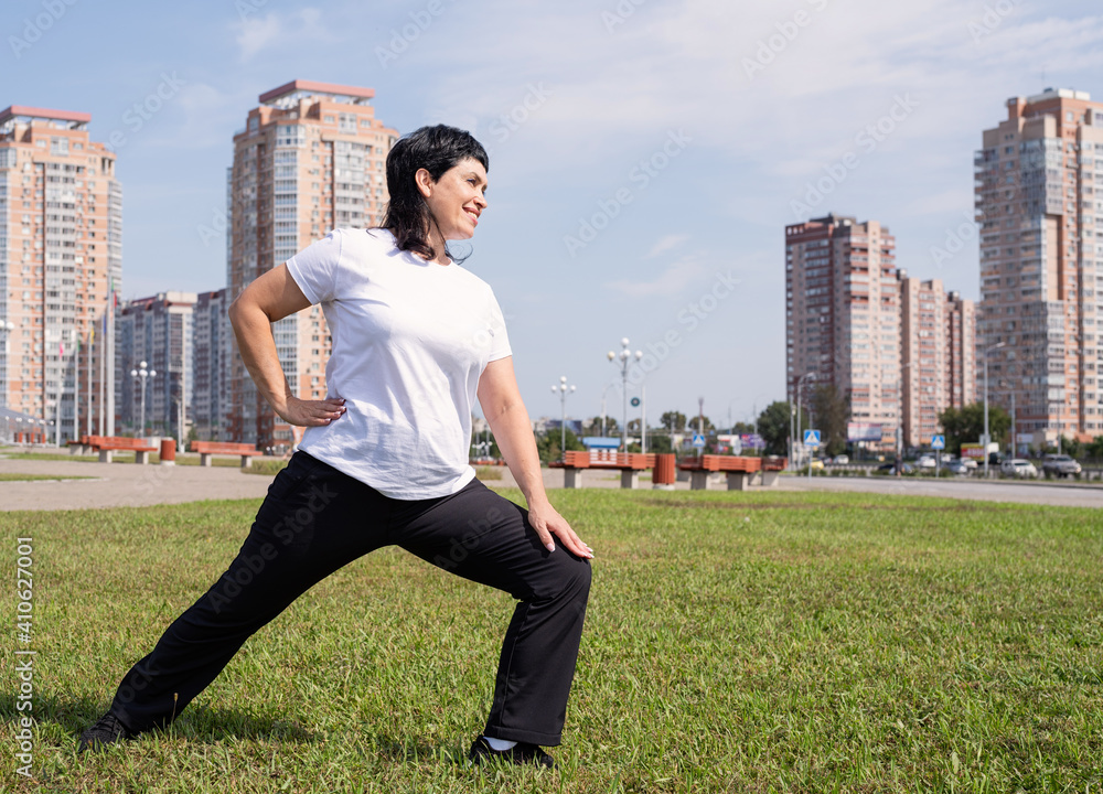 Smiling senior woman warming up stretching outdoors in the park