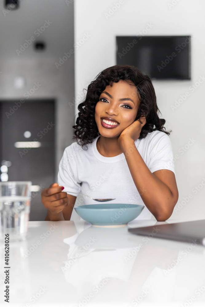Young healthy laughing african woman eating breakfast and fruits in kitchen in the morning. Breakfast Young healthy laughing african woman eating breakfast and fruits in kitchen in the morning. Breakfast