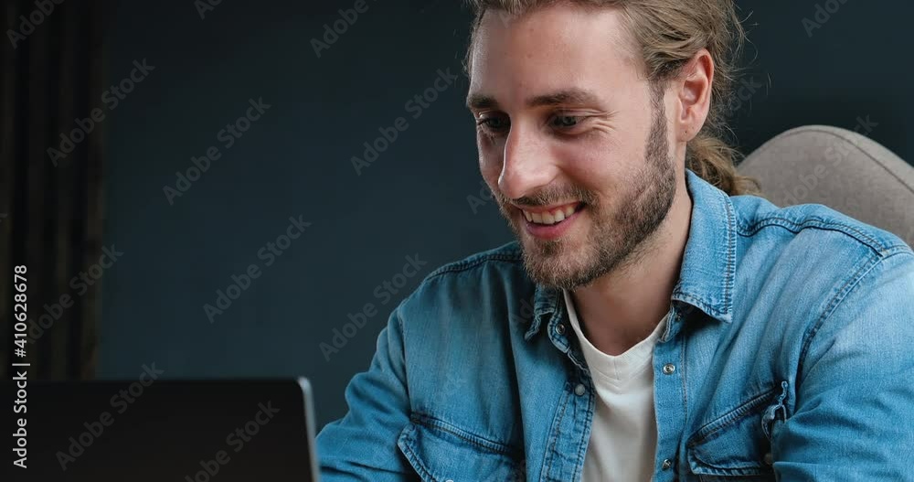 Young Man is chatting with Friends on Laptop, browsing Social Networks. Happy Man is texting Messages on his PC in Loft Living Room at Home. Online Surfing Lifestyle. Freelance People. Young Man is chatting with Friends on Laptop, browsing Social Networks. Happy Man is texting Messages on his PC in Loft Living Room at Home. Online Surfing Lifestyle. Freelance People.