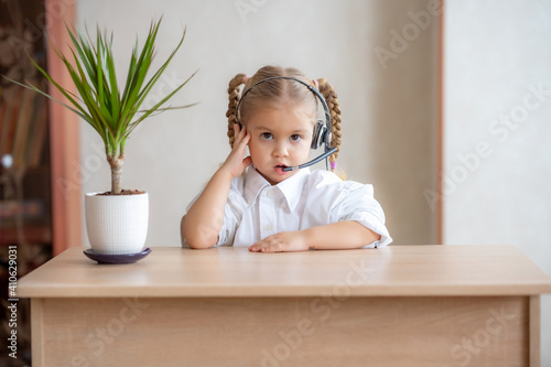 pretty little girl sitting at table, wearing headphones with mic, looking at camera.