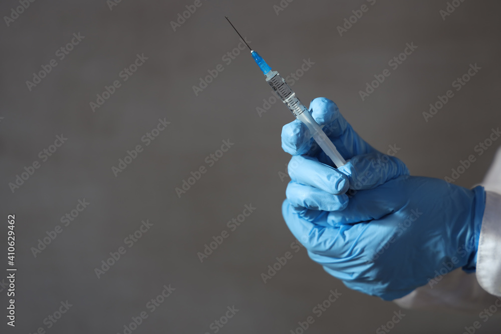 Doctor's hands in medical gloves hold a syringe for revaccination against omicron strain on gray background. Doctor's hands in medical gloves hold a syringe for revaccination against omicron strain on gray background.