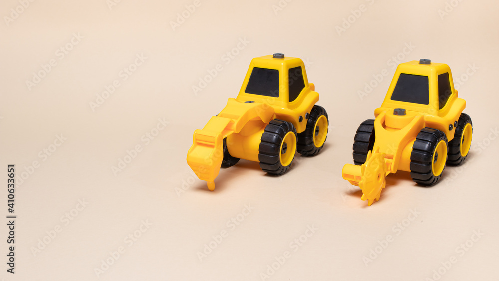 Two yellow construction tractors on a light beige background. Cars for children and toy store Two yellow construction tractors on a light beige background. Cars for children and toy store