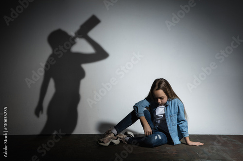 Fototapeta Naklejka Na Ścianę i Meble -  Domestic physical violence, abusing. Scared little caucasian girl, victim sitting close to white wall with shadow of angry threatening mother with alcohol addiction. Awareness of social problem.