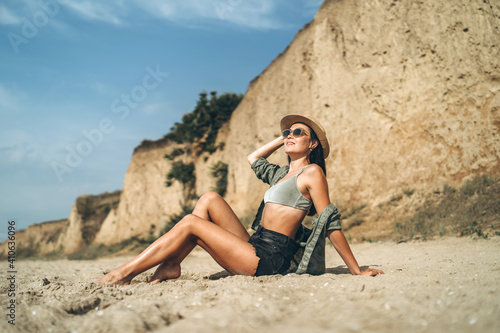 Brunette girl in hat relaxing on the beach with rocks on background.