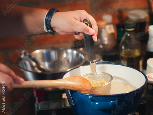Hand-holding the colander of the spaghetti in a pot with boiling water to prepare cooking in the kitchen. Close-up photo. Foods concept