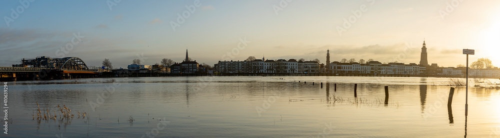 Reflection in super wide panoramic landscape with the river IJssel overflowing its boundaries into floodplains because of high water levels and silhouette cityscape of Zutphen in The Netherlands