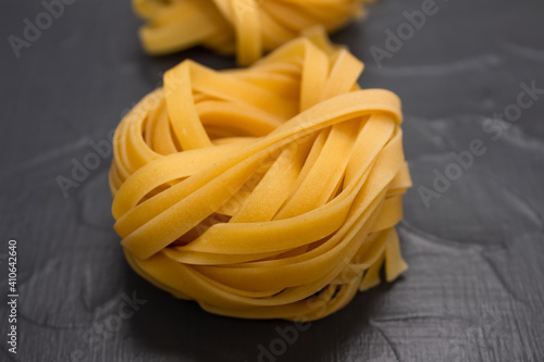 Close up of homemade tagliatelle nests, yellow pasta over gray stone background with copy space. Italian food in colors of the year 2021. Fresh homemade or semi finished food, selective focus