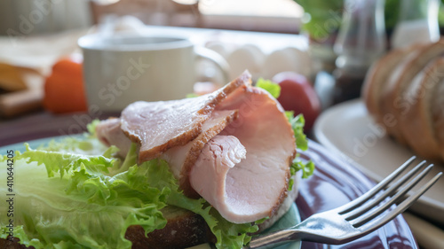 Sandwich with ham and green salad on a plate. Kitchen table. Breakfast. Close-up. Soft focus in the background