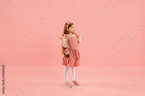 Astonished. Childhood and dream about big and famous future. Pretty longhair girl on coral pink studio background. Childhood, dreams, imagination, education, facial expression, emotions concept.