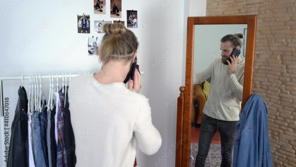 Attractive Young Stylish man in a long sleeves is looking in a mirror Talking on the smartphone Choosing shirt Attractive Young Stylish man in a long sleeves is looking in a mirror Talking on the smartphone Choosing shirt