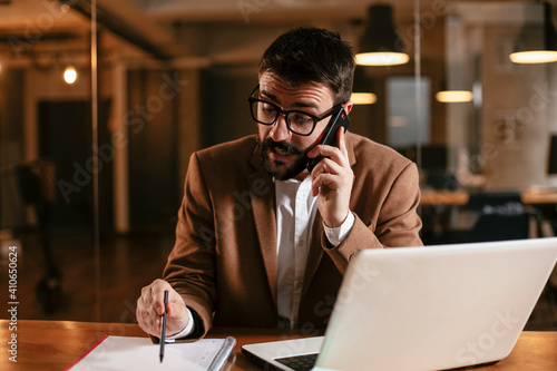 Handsome man talking to the phone at his workplace. Young businessman using laptop in his office..