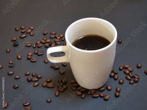 Close up of a white cup of coffee and roasted coffee beans on black background