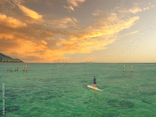 A sunset view with a guy was doing a paddleboard over the beach. 