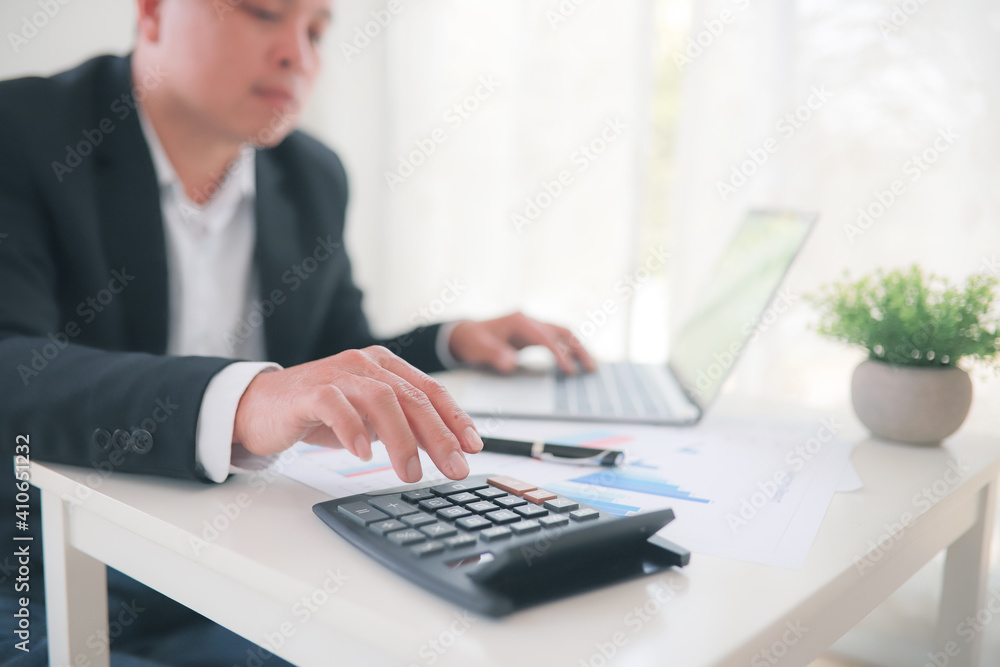 teamwork business man accounting working financial concept in office,Man in a blue suit typing on the calculator and working on a white laptop on the working desk. teamwork business man accounting working financial concept in office,Man in a blue suit typing on the calculator and working on a white laptop on the working desk.