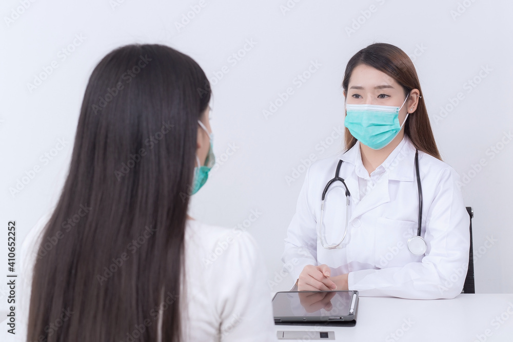 Asian woman patient consults her health with doctor, doctor give counsel with her while both wear medical face mask to protect infection disease in hospital. Coronavirus protection concept. Asian woman patient consults her health with doctor, doctor give counsel with her while both wear medical face mask to protect infection disease in hospital. Coronavirus protection concept.