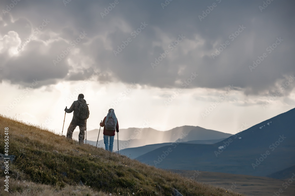 Two hikers stands on mountain slope against sunset