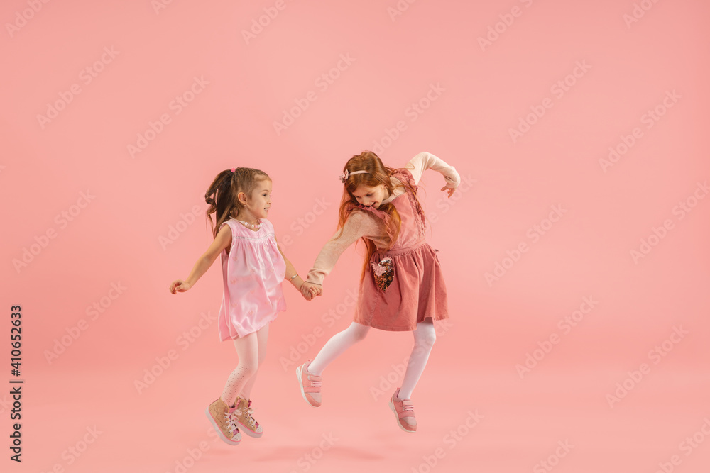 Running. Childhood and dream about big and famous future. Pretty little girls on coral pink studio background. Childhood, dreams, imagination, education, facial expression, emotions concept. Running. Childhood and dream about big and famous future. Pretty little girls on coral pink studio background. Childhood, dreams, imagination, education, facial expression, emotions concept.