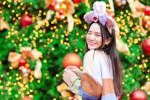 Photography An Asian girl in a colorful sweater stands in front of the Christmas tree