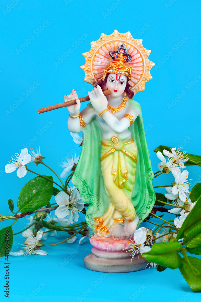 Hindu god Krishna. Statue with white cherry flowers on a blue background.