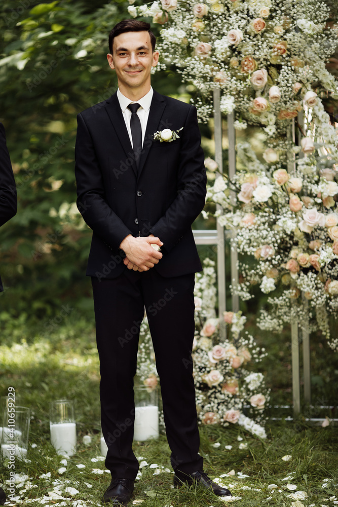 the groom stands near the altar. wedding ceremony where the happy groom is waiting for the bride. wedding day. groom in black suit at the exit ceremony the groom stands near the altar. wedding ceremony where the happy groom is waiting for the bride. wedding day. groom in black suit at the exit ceremony