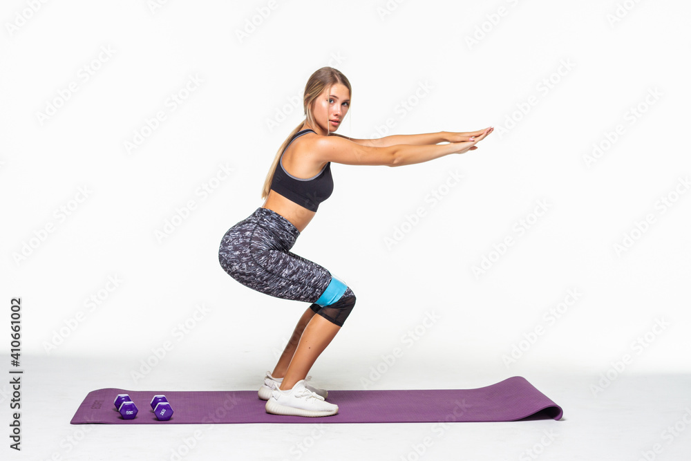 Slim woman doing squats with fitness loop band isolated on white background Slim woman doing squats with fitness loop band isolated on white background