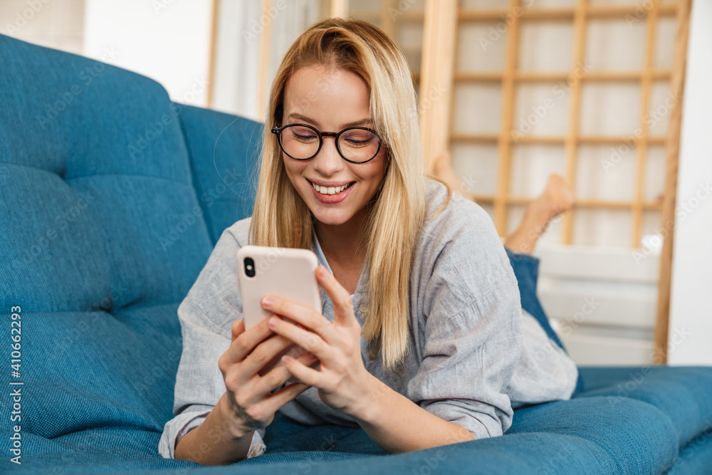Smiling blonde woman using mobile phone while lying on couch Smiling blonde woman using mobile phone while lying on couch