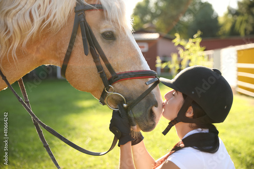 Young woman in horse riding suit and her beautiful pet outdoors on sunny day