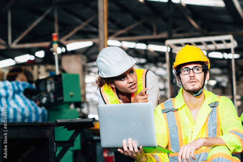 Fototapeta premium Work at factory.engineer woman and workers man team working together in safety work wear with white and yellow helmet using laptop computer.in factory workshop industry meeting professional