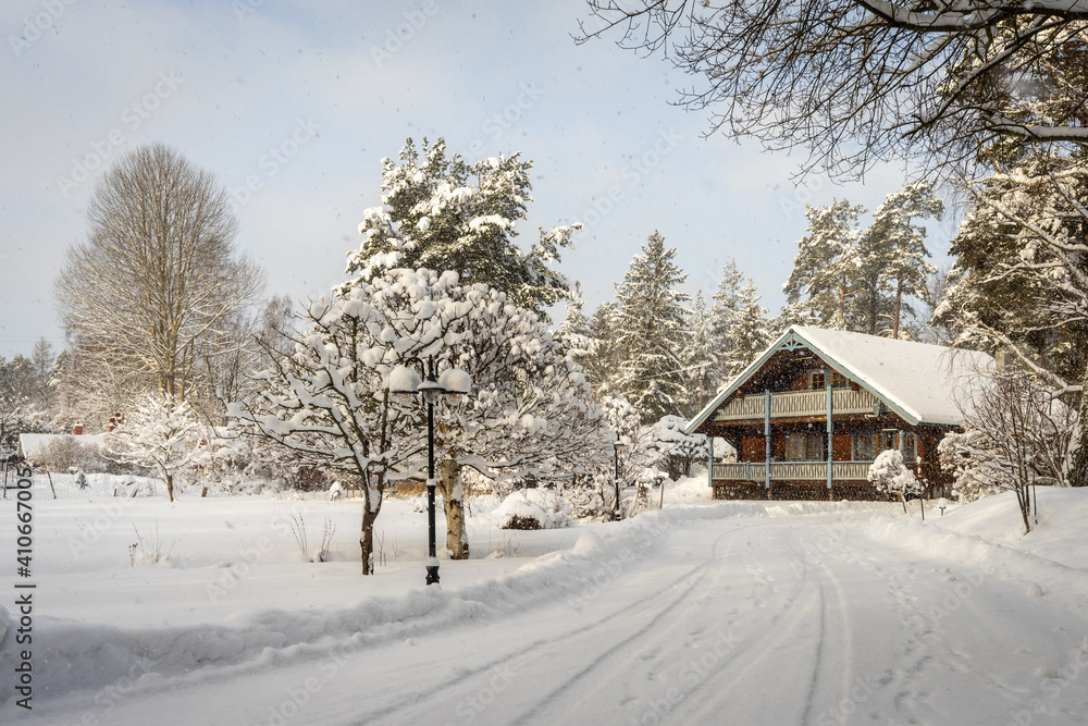 Beautiful wooden two storey chalet house with carved decorative elements. Balcony terrace for relax in countryside house. Delightful snowy landscape of house surrounded by woods. Ecological settlement