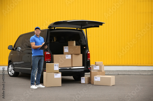 Courier with clipboard and parcels near delivery van outdoors photo