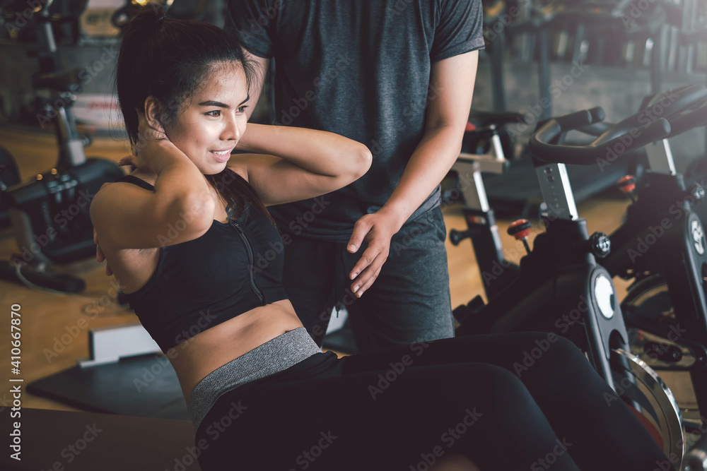 Asian woman work out with a personal trainer doing sit ups to stay healthy at the gym.
