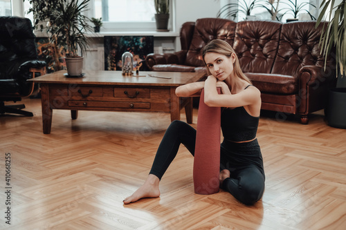 Caucasian fitness woman sitting on floor with mat poses in beautiful apartment in retro style in daytime.