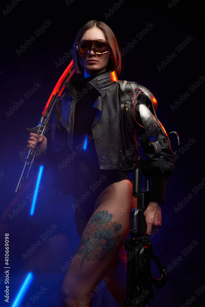 Obraz premium Fantasy portrait of a attractive female soldier with short haircut holding a futuristic sword on her shoulder and gun. Dangerous woman in cyberpunk style going in dark background.