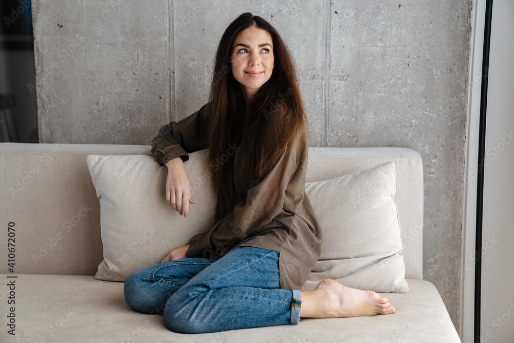 Happy brunette nice girl smiling while sitting on sofa at home Happy brunette nice girl smiling while sitting on sofa at home