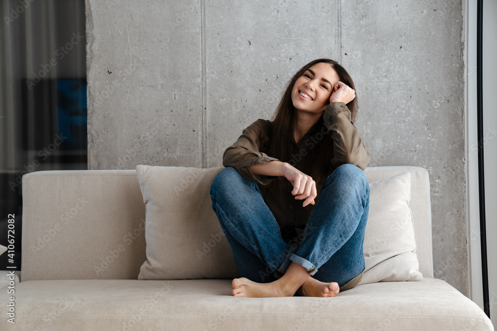 Happy brunette nice girl smiling while sitting on sofa at home Happy brunette nice girl smiling while sitting on sofa at home